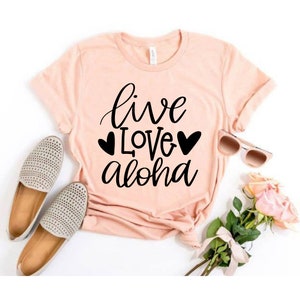 May include: A pink t-shirt with the text "live love aloha" in black lettering with two black hearts on either side of the word "love".