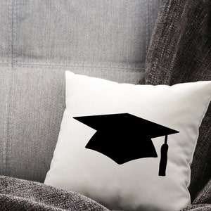 May include: A white pillow with a black silhouette of a graduation cap.