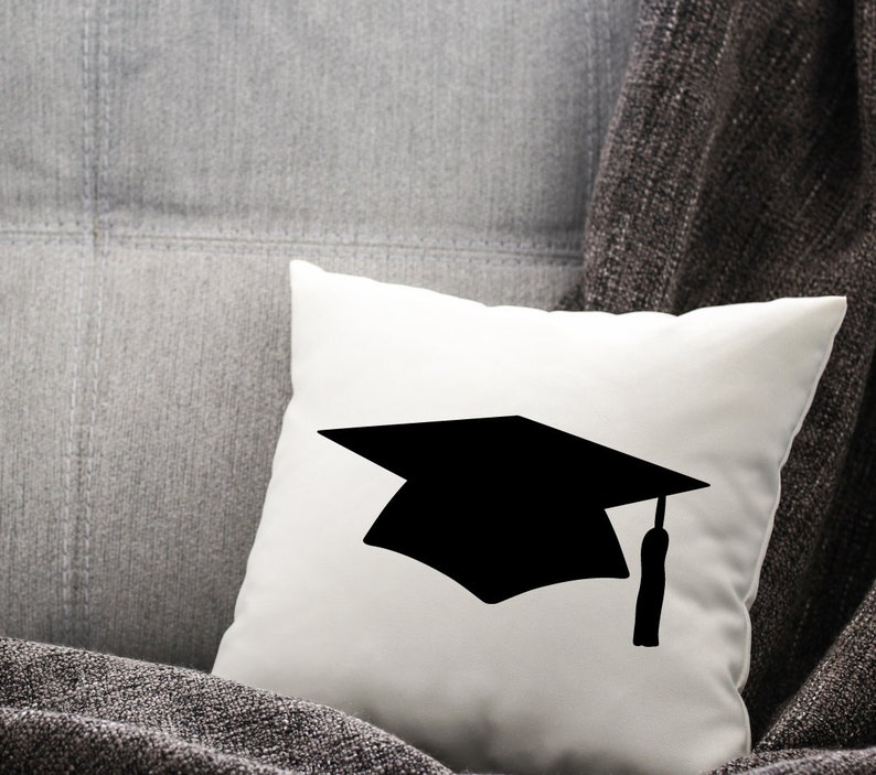 May include: A white pillow with a black silhouette of a graduation cap.