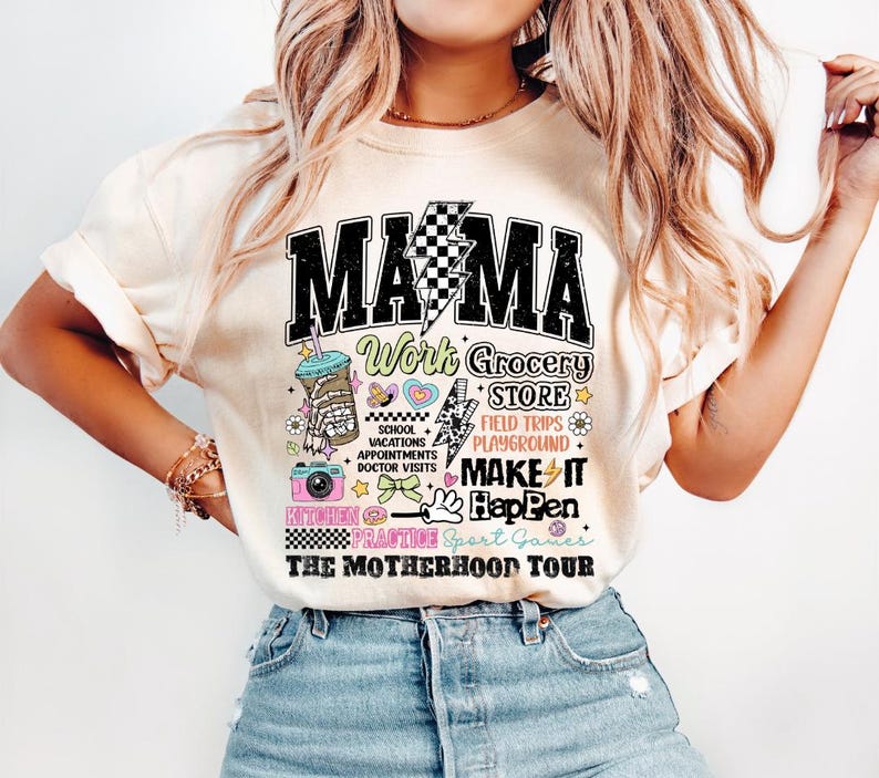 May include: A white t-shirt with a black graphic that says "Mama" and features a variety of colorful illustrations, including a coffee cup, a camera, a donut, and a lightning bolt. The text on the graphic says "Work Grocery Store, School Vacations Appointments Doctor Visits, Field Trips Playground, Make It Happen, Kitchen Practice Sport Games, The Motherhood Tour."