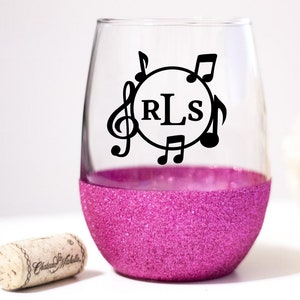 May include: A pink glitter stemless wine glass with a black vinyl decal of musical notes and the monogram "RLS".