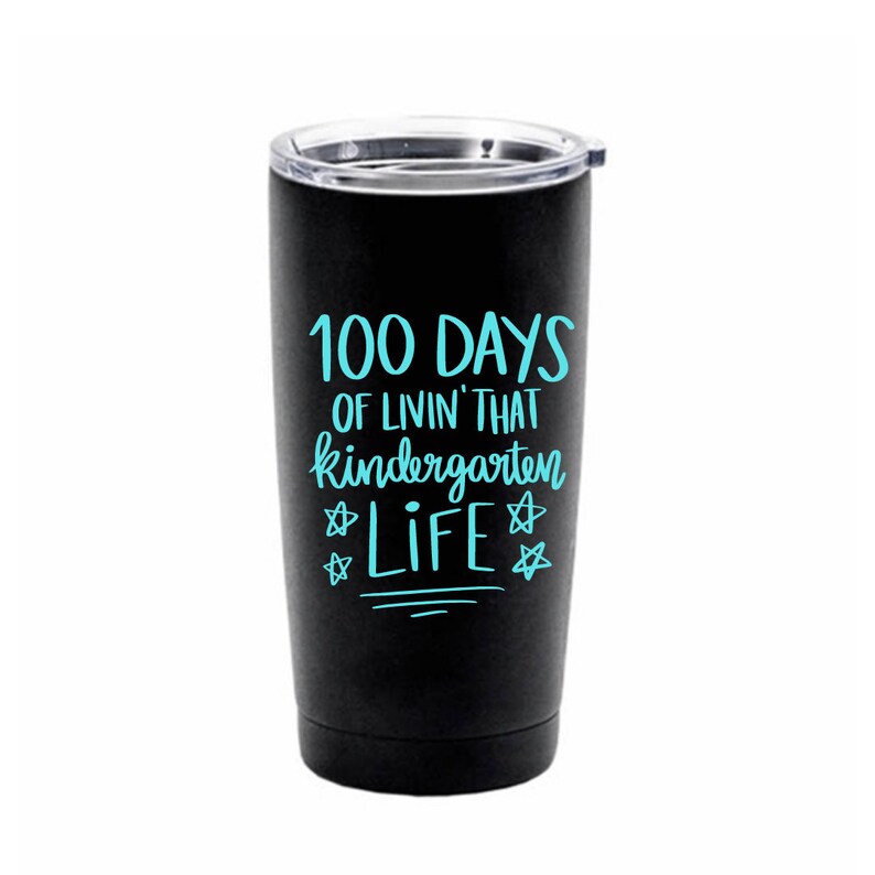 May include: Black stainless steel tumbler with a blue inscription that reads "100 Days of Livin' That Kindergarten Life" with stars on either side of the word "Life".