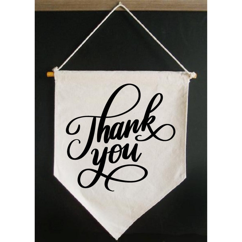 May include: A white canvas banner with a black cursive inscription that reads "Thank you". The banner is hanging from a string and has a wooden dowel rod at the top.