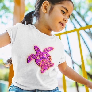 K&ouml;nnte beinhalten: Ein wei&szlig;es T-Shirt mit einem pinkfarbenen und violetten Muster einer Meeresschildkr&ouml;te. Die Schildkr&ouml;te ist nach rechts im Bild ausgerichtet.