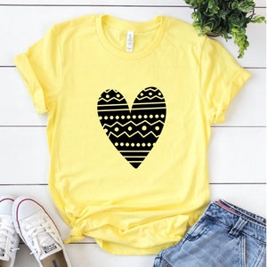 May include: A yellow t-shirt with a black heart design. The heart is filled with a geometric pattern of black and white lines, dots, and zigzags.