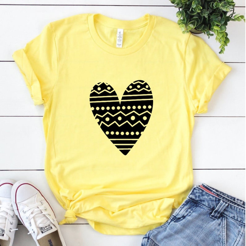 May include: A yellow t-shirt with a black heart design. The heart is filled with a geometric pattern of black and white lines, dots, and zigzags.