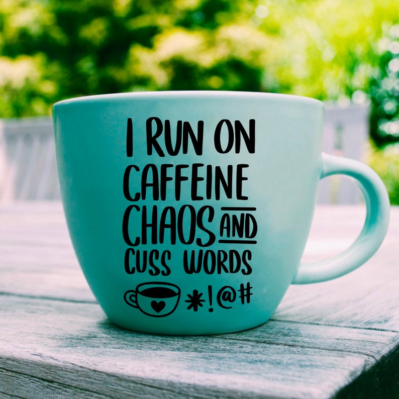 May include: A light blue ceramic coffee mug with a black graphic that reads "I run on caffeine chaos and cuss words *!@#".