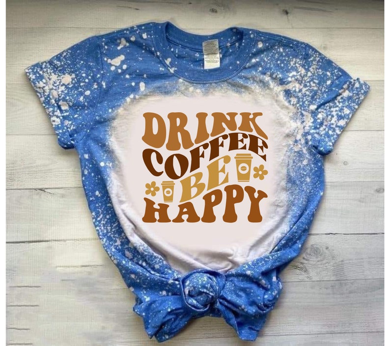 May include: A white t-shirt with a blue bleach splattered design. The shirt has a brown graphic that says "Drink Coffee Be Happy" with coffee cup illustrations.