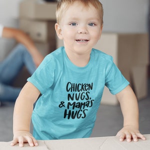 May include: A young child wearing a turquoise blue t-shirt with the text "Chicken Nugs. & Mamas Hugs" printed in black.