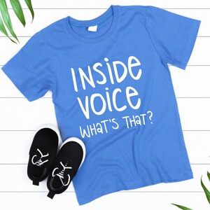 May include: A blue t-shirt with white text that reads "Inside voice What's that?"