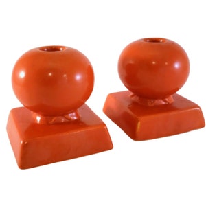 May include: A pair of orange ceramic candle holders with a round top and a square base.