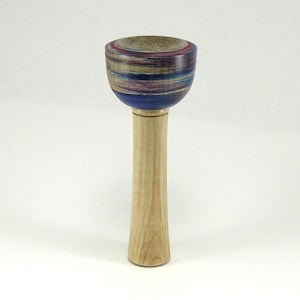 May include: A handcrafted wooden bowl with a long, slender stem. The bowl features a colorful, layered design with shades of blue, red, and tan. The stem is made of light-colored wood. The bowl is likely used for decorative or ceremonial purposes.