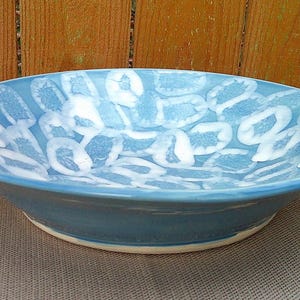 Op de afbeelding: Een grote, blauwe keramische kom met een wit, abstract ontwerp. De kom is geglazuurd en heeft een licht afgeronde rand.
