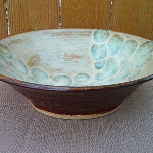 May include: A large, ceramic serving bowl with a brown rim and a white interior. The bowl has a unique design of blue and green speckled glaze.