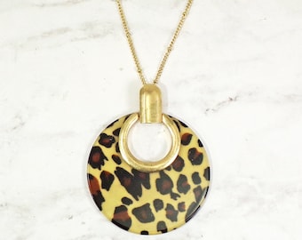 Grande pendente rotondo con stampa animalier, realizzato in acrilico piatto di colore marrone e sospeso a una lunga catena dorata.