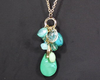 Green beaded tassel necklace made with shell, glass, and acrylic beads in a cluster tassel suspended from a gold ring, and link chain.