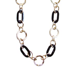 Puede incluir: Un collar de cadena dorada con eslabones ovalados y redondos negros.