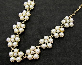Pearl flower necklace designed with white faux pearls.  It has nine pearl flower stations linked together in gold tone settings.