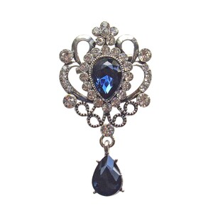 Broche de diseño vintage "Reina de Cristal Azul" con cristal azul en forma de lágrima, cristales transparentes y detalles ornamentales con cristales redondos.