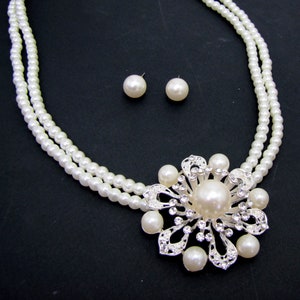 Larger round pearl pendant with white faux pearls and clear crystals set onto the pendant and attached to a double row of white glass pearls