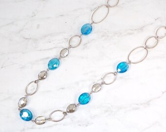 Long glass beaded necklace with a mix of light blue and gray glass beads. It is designed with oval glass beads and large oval silver links