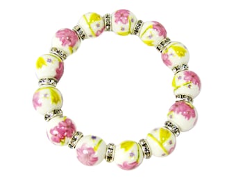 Pode incluir: Um bracelete de cerâmica branca com desenhos florais rosa e amarelo e detalhes prateados.