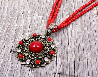 Round pendant necklace with red beads and clear crystals and it is attached to two rows of a red wood beaded necklace.