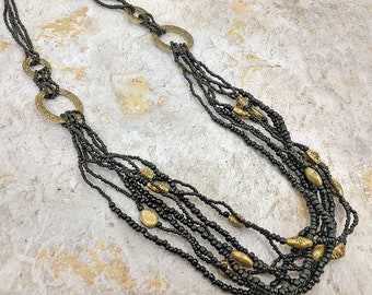 Collana multi strand a strati di semi neri con antichi collegamenti di finitura oro, lunga collana di semi neri multifilamento.
