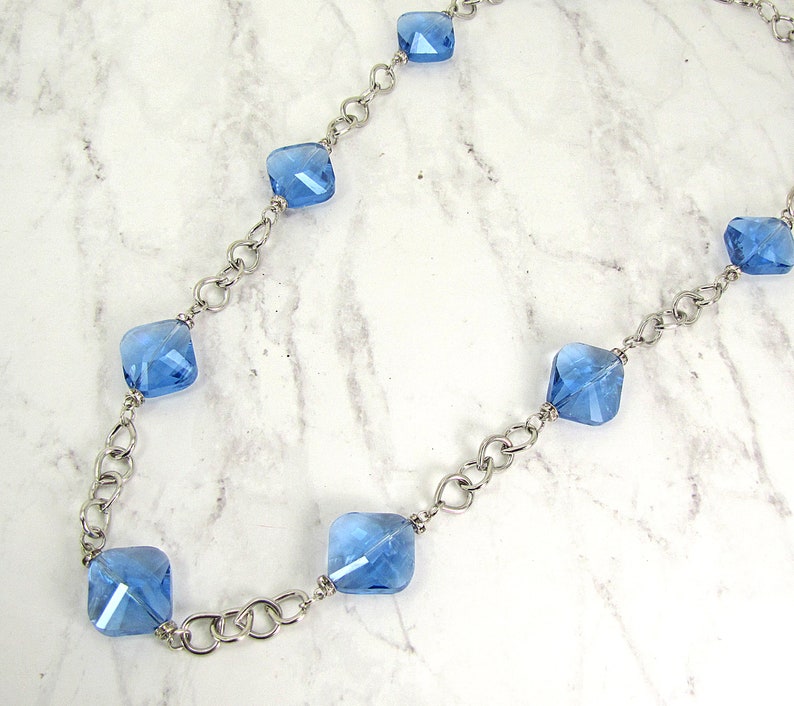 Each glass bead is accented with small crystal spacer beads. Long blue glass beaded necklace with silver plated tear drop shape links