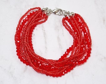 Rode meerstrengige armband met glaskralen en rocailles gemaakt met negen strengen rode kralen. Rode modieuze armband.