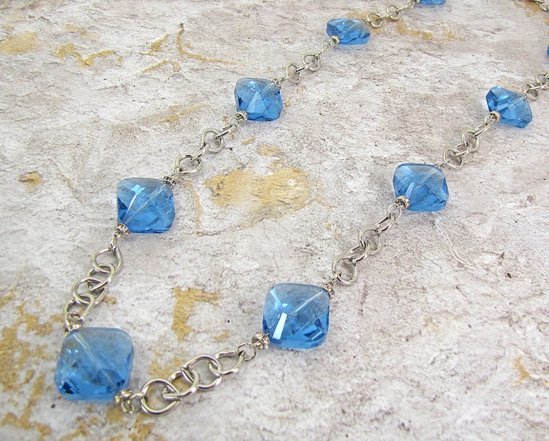 Each glass bead is accented with small crystal spacer beads. Long blue glass beaded necklace with silver plated tear drop shape links