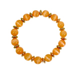 May include: An orange beaded bracelet with gold-coloured accents. The bracelet features large, round, orange beads separated by small, gold-coloured, circular spacers. The beads have a translucent quality, set against a white background.