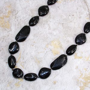 Könnte beinhalten: Eine schwarze Halskette mit großen, ovalen Perlen. Die Perlen haben ein marmoriertes Muster mit weißen Streifen.
