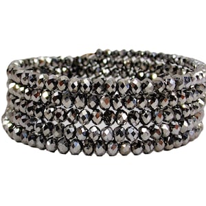 May include: A silver beaded bracelet with multiple strands of faceted beads. The bracelet is made of small, round beads that are tightly woven together.