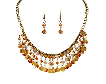 Conjunto de collar y pendientes con flecos de cuentas de vidrio en tonos naranja y crema. Joyas llamativas con un estilo bohemio y elegante.