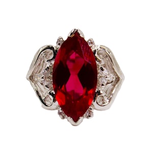 May include: A silver ring with a large, red, marquise-shaped gemstone surrounded by smaller, clear gemstones.