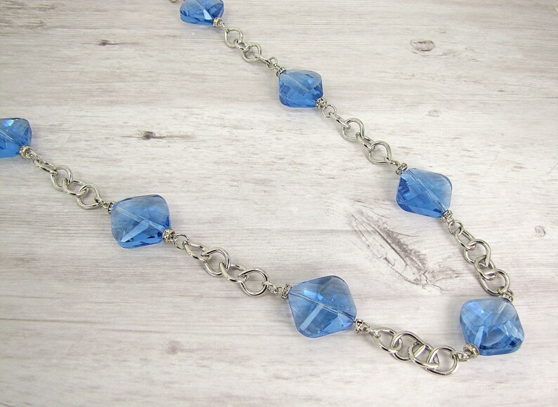 Each glass bead is accented with small crystal spacer beads. Long blue glass beaded necklace with silver plated tear drop shape links