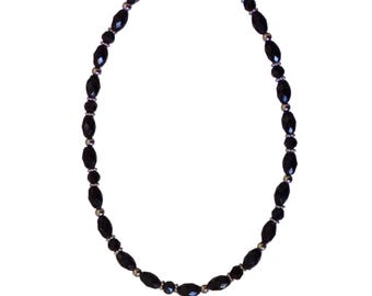 Collana di perline nere e argentate realizzata con perline acriliche a forma di tubo e perline di vetro a forma di rondella, abbinate a perline rotonde argentate.