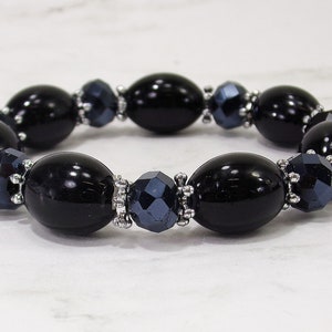Black glass beaded stretch bracelet with silver plated spacer beads.  It is designed with smooth oval and rondelle shape black glass beads.