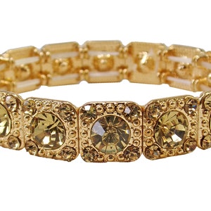 May include: A gold bracelet with a stretchy band and square-shaped, clear, light yellow rhinestones.