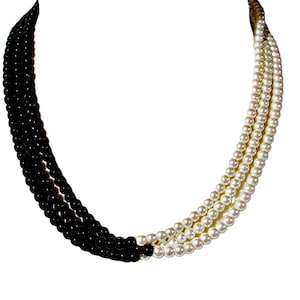 May include: A multi-strand necklace featuring a striking contrast of black and white beads. The necklace is composed of three strands of black beads and three strands of white beads, creating a bold and elegant design. The necklace is set against a white background.