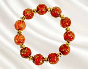 Bracciale elastico con perline rosse e dorate, perline in resina con foglia d'oro e perline distanziatrici placcate in oro.