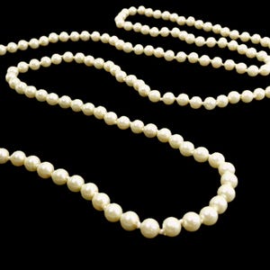 Peut inclure: Un long collier de perles blanches, enfilées sur un fil fin. Les perles sont de taille et de forme uniformes, et ont une finition lisse et brillante.