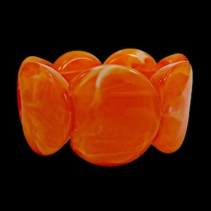 May include: Orange and white marbled stretch bracelet. The bracelet features large, rounded, oval-shaped beads. The beads are a vibrant orange with white marbling, set against a black background. The bracelet is a bold statement piece.