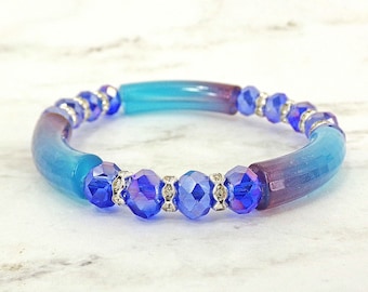 Bracelet extensible en perles de verre bleues et violettes mélangées à des espaceurs en cristal incolore. Il est conçu avec des perles de verre rondes et tubulaires.