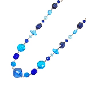 Long blue glass beaded necklace designed with a mix of light and dark blue color beads in various shapes linked together.