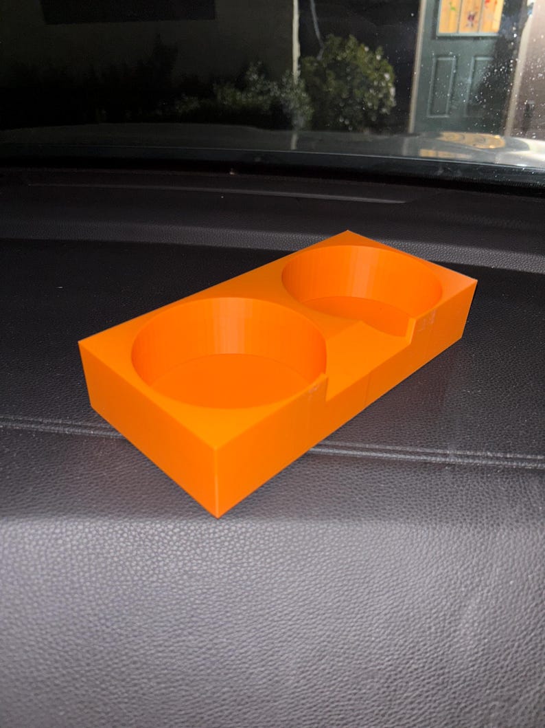 Puede incluir: Portavasos de coche de color naranja brillante con dos aberturas circulares y una base rectangular. El portavasos est&aacute; hecho de un material s&oacute;lido y est&aacute; dise&ntilde;ado para sostener dos bebidas. El dise&ntilde;o es simple y funcional.