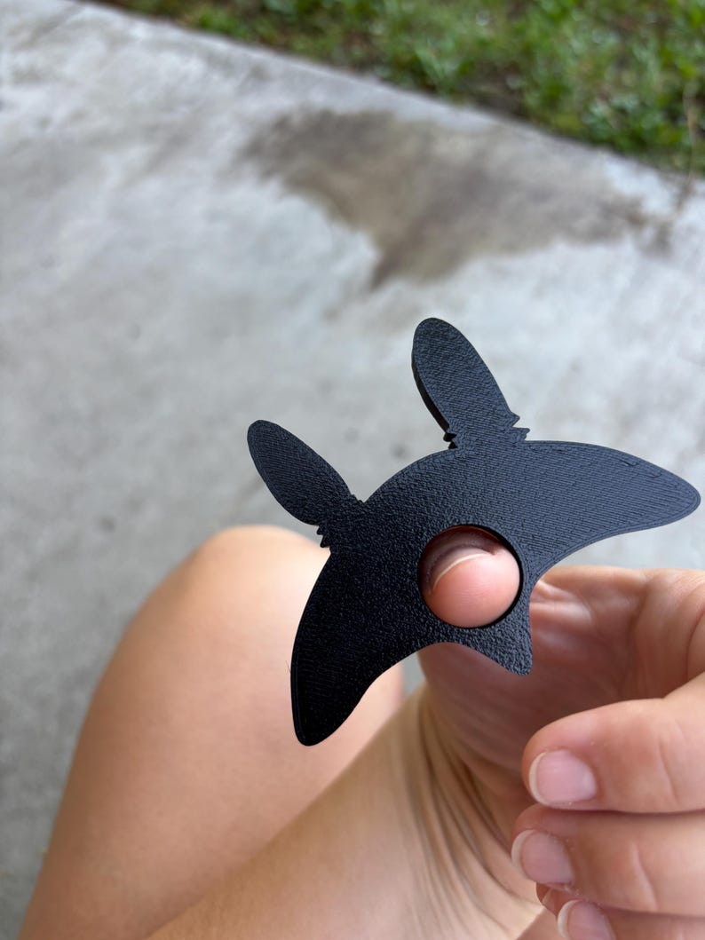 May include: A black metal star-shaped object with a circular hole and two upward protrusions. The object is held in a hand. The background is blurred.
