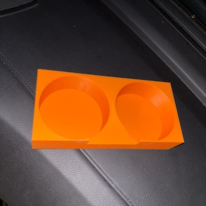 Puede incluir: Portavasos de coche de pl&aacute;stico naranja brillante con dos aberturas circulares. El soporte rectangular tiene una base plana y est&aacute; dise&ntilde;ado para sostener dos tazas o botellas. El portavasos est&aacute; hecho de un material s&oacute;lido y duradero.