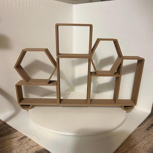 May include: A brown wooden shelf unit with geometric shapes, including a square, hexagon, and rectangle. The shelf unit is on a white surface.